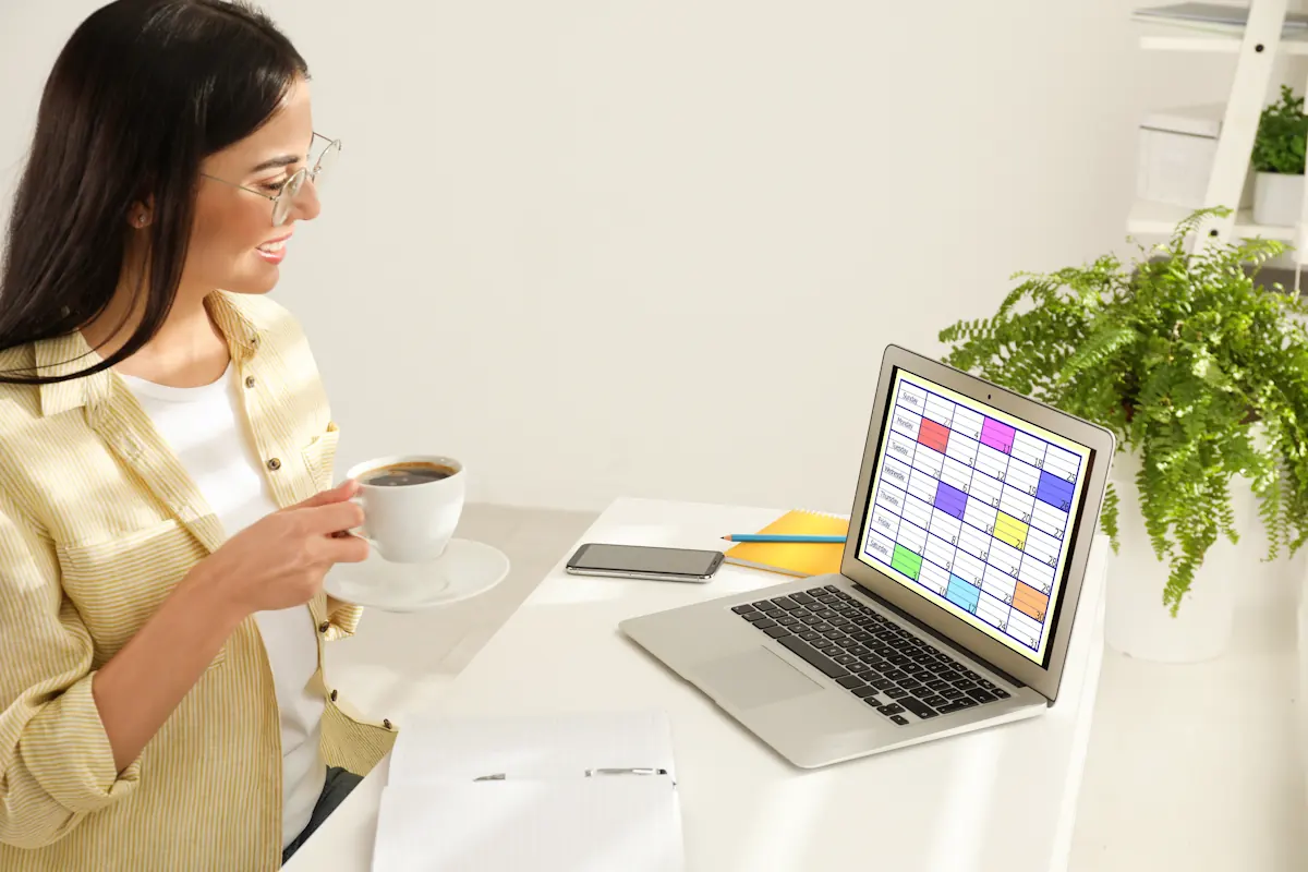Une femme avec une tasse à la main qui regarde son ordinateur et ses fichiers prospects CRM